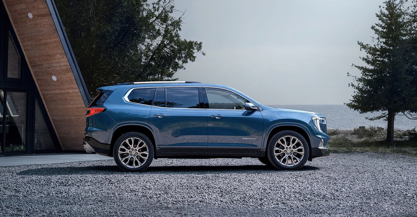GMC ACADIA parked beside a modern cabin near a lake or coastal area.