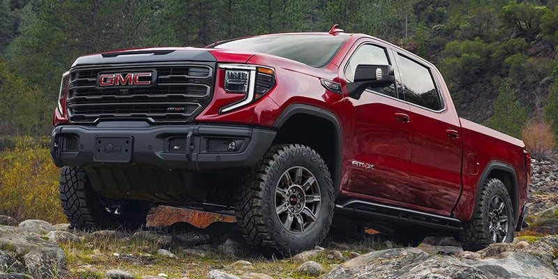 GMC Sierra AT4X parked on rocky terrain surrounded by trees and mountains.