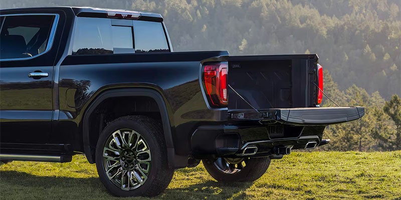 Rear view of GMC truck with tailgate open, parked on grassy terrain.