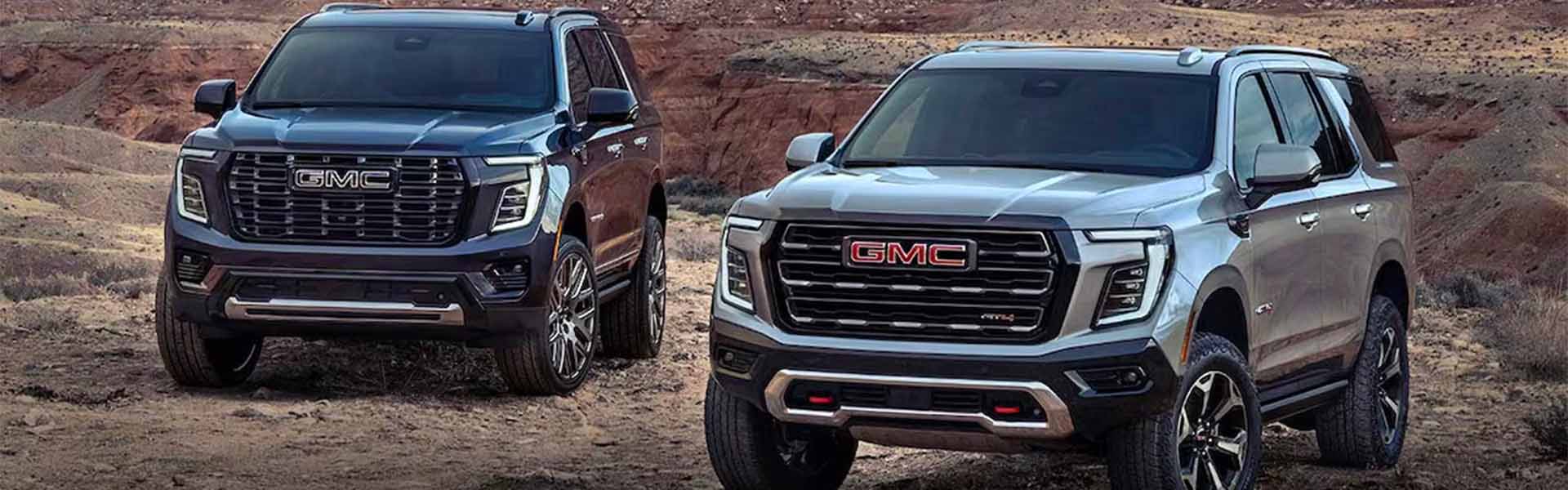 Two GMC SUVs parked in a rugged desert landscape, showcasing bold front grilles.