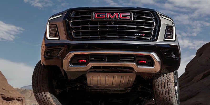 Close-up of lifted GMC front grille and bumper in rugged off-road terrain.