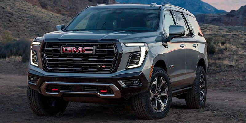 GMC AT4 SUV parked on rugged terrain during sunset, showcasing bold front design.
